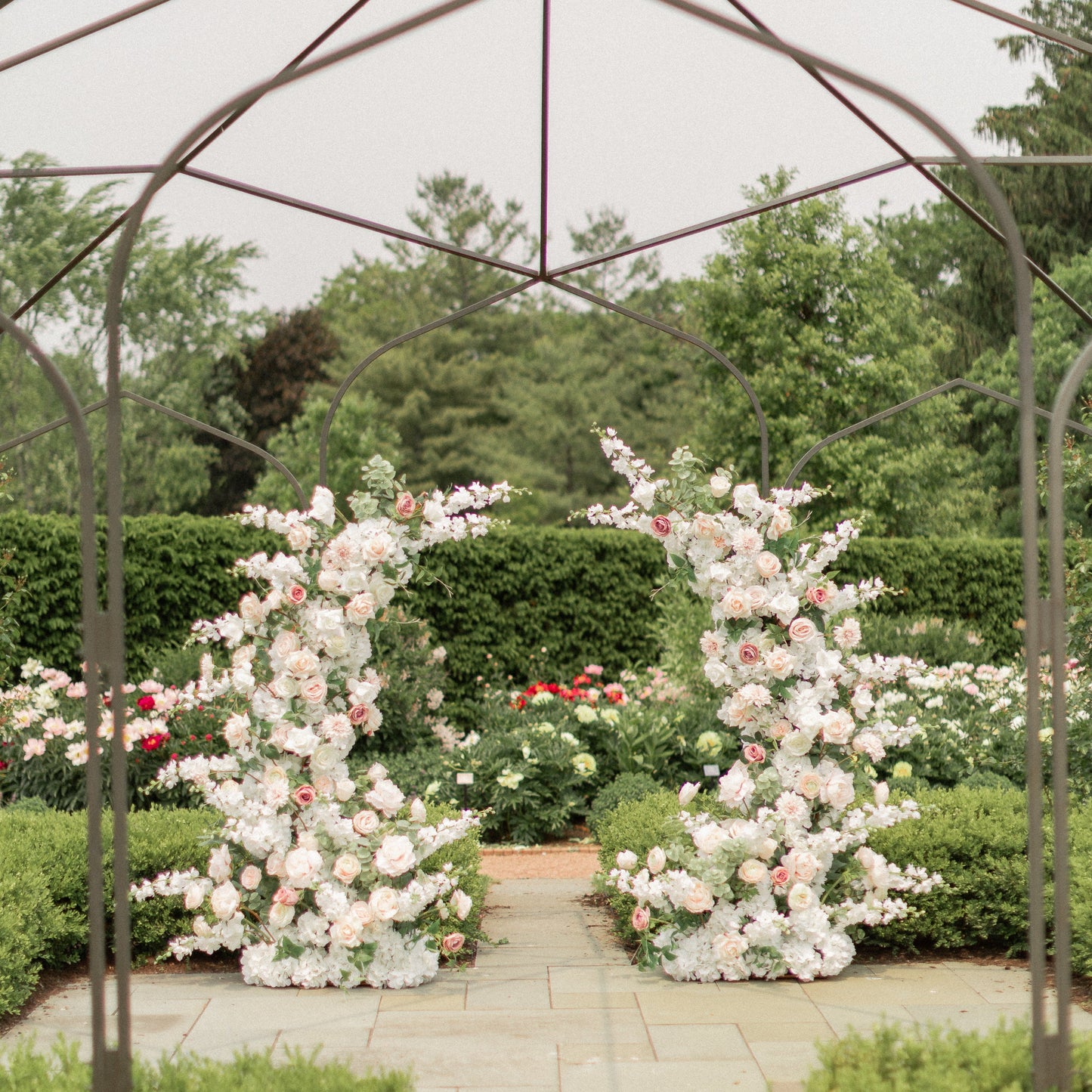 Floral archway at a garden wedding venue with metal pergola and greenery.