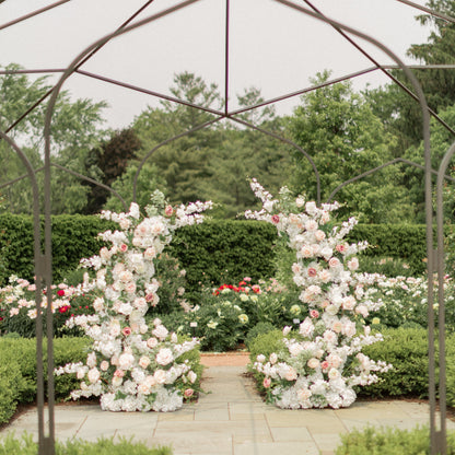 Floral archway at a garden wedding venue with metal pergola and greenery.