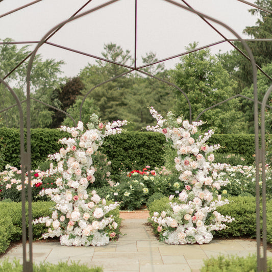 Floral archway at a garden wedding venue with metal pergola and greenery.